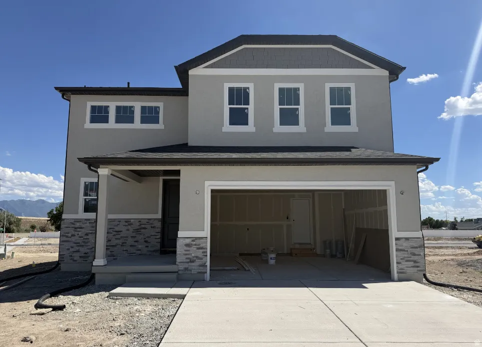 Two-story stucco residence featuring a dual-car garage, stone veneer accents, and a covered porch entry