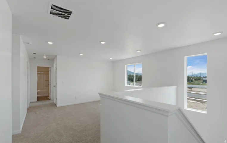 Recessed lighting, white walls, carpeted flooring, two windows, and a white staircase with a railing