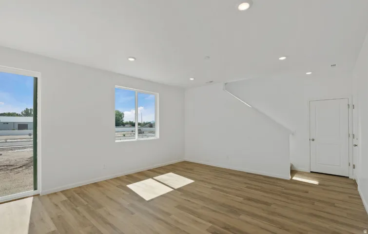 Recessed ceiling lighting, wood-finish flooring, white walls, double-pane window, and a sliding glass door