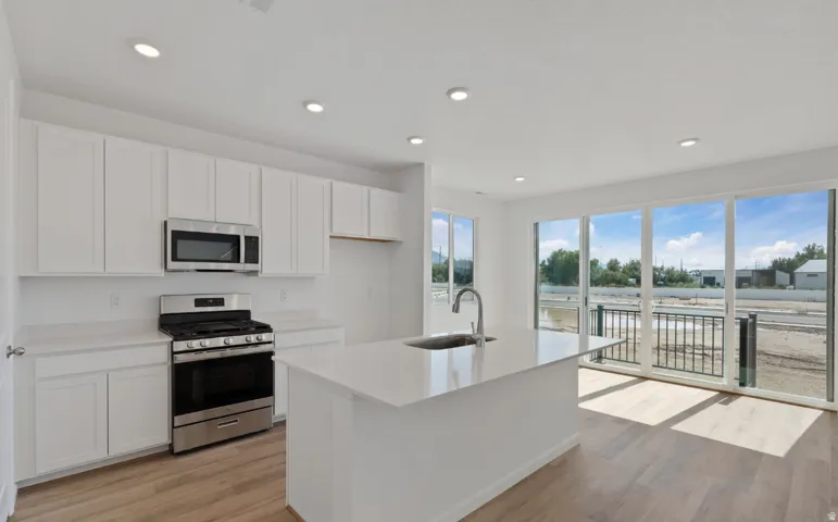 White shaker cabinetry, stainless steel appliances, a center island with an undermount sink, and wood-finish flooring