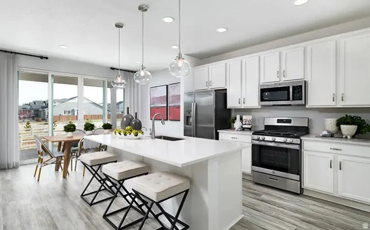 Spacious kitchen featuring white cabinetry, stainless steel appliances, a center island with pendant lighting, and wood-finish flooring