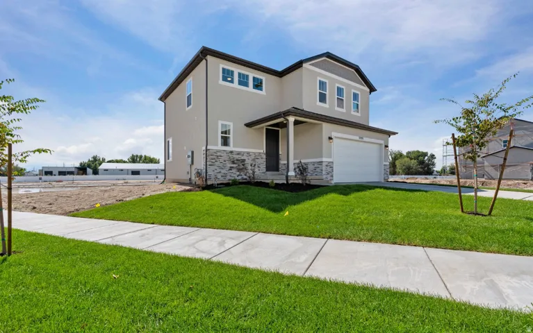 Two-story stucco exterior with stone accents, covered entry, attached garage, and established lawn