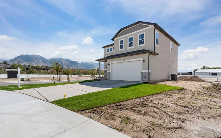 Stucco exterior with stone accent siding, attached two-car garage, concrete driveway, and front lawn