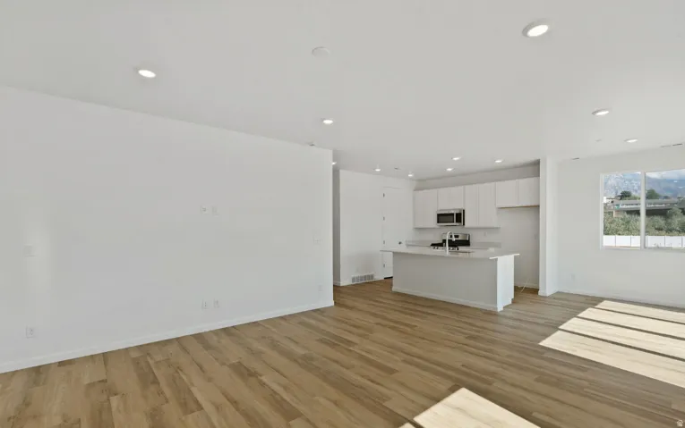 Open-concept living space featuring wood-finish flooring, recessed lighting, and a kitchen with white cabinetry and a central island