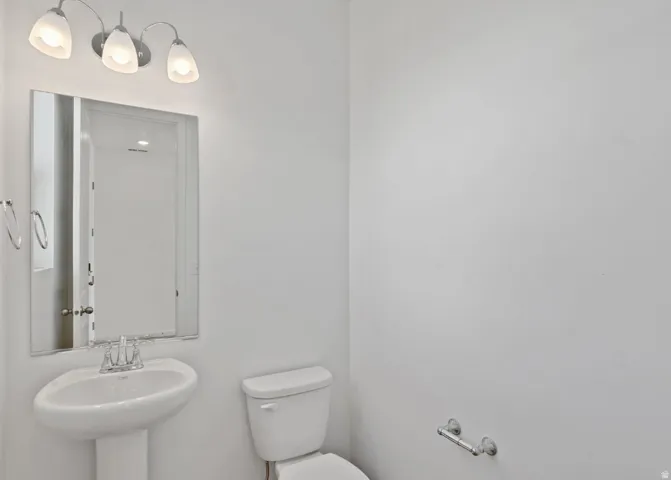 Pedestal sink with chrome faucet, wall-mounted mirror, and vanity light fixture