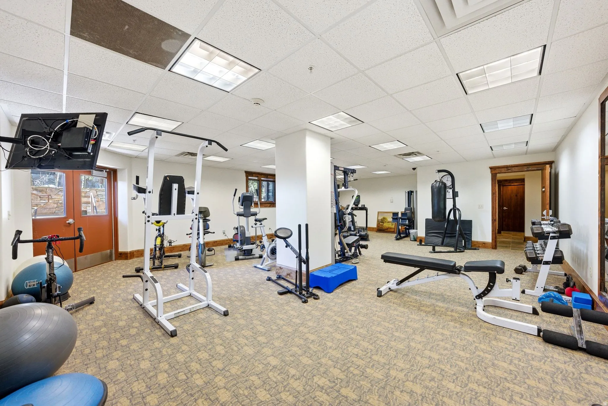 Spacious fitness room featuring patterned carpeting, recessed lighting, a drop-panel ceiling, and multiple workout equipment stations