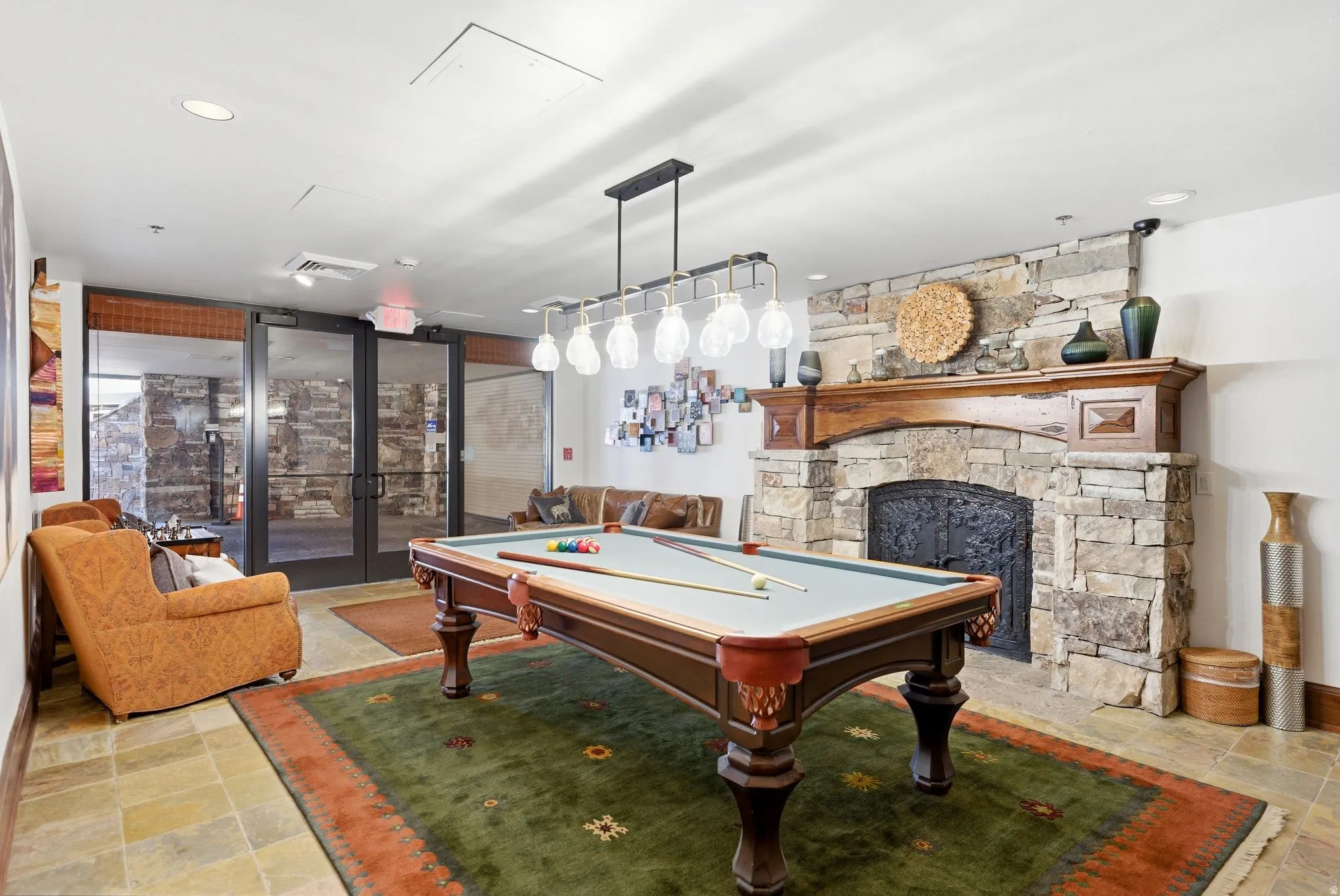 Recreational room featuring a stone-clad fireplace with a wood mantel, slate flooring, and a multi-bulb chandelier