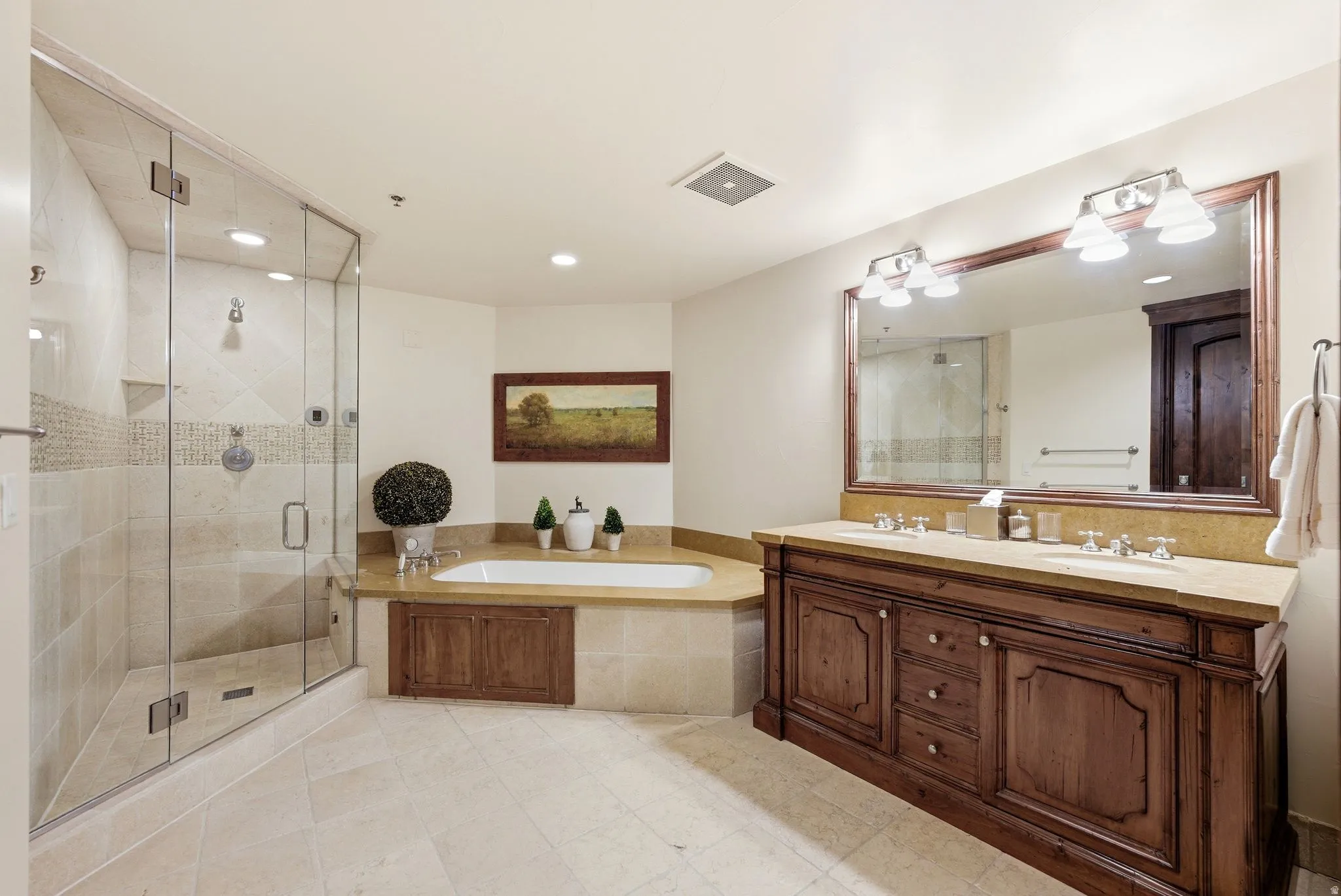 Spacious bathroom featuring a glass-enclosed shower, a built-in tub with stone surround, a dual vanity with wood cabinetry and stone countertop, and large format floor tiling
