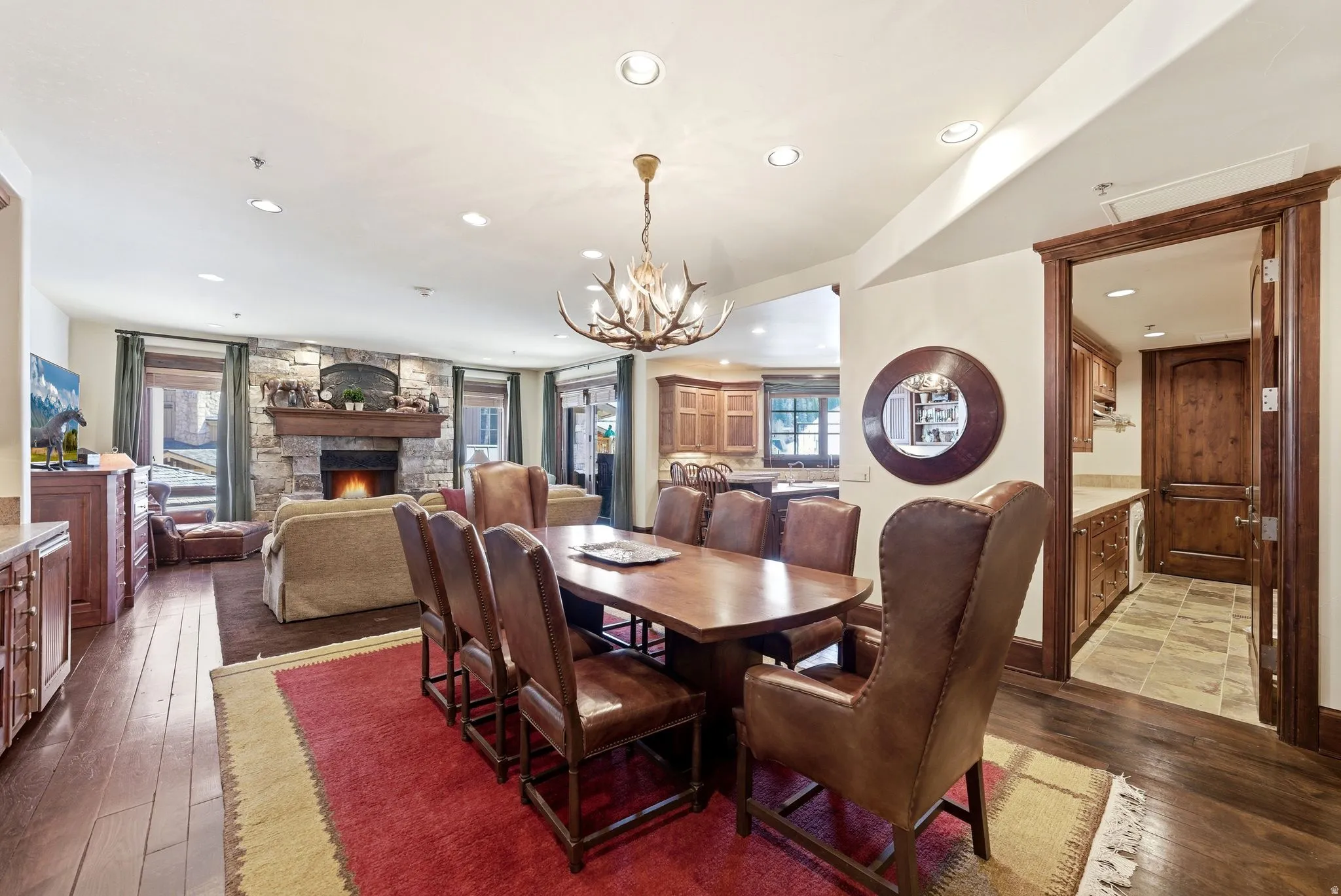 Open concept living area featuring wood-finish flooring, a stone fireplace with a substantial wood mantel, a distinctive antler chandelier, recessed lighting, and a defined dining space