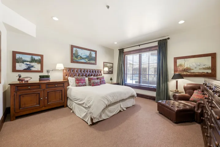 Carpeted room featuring a tufted leather headboard and a window with wood-finish trim