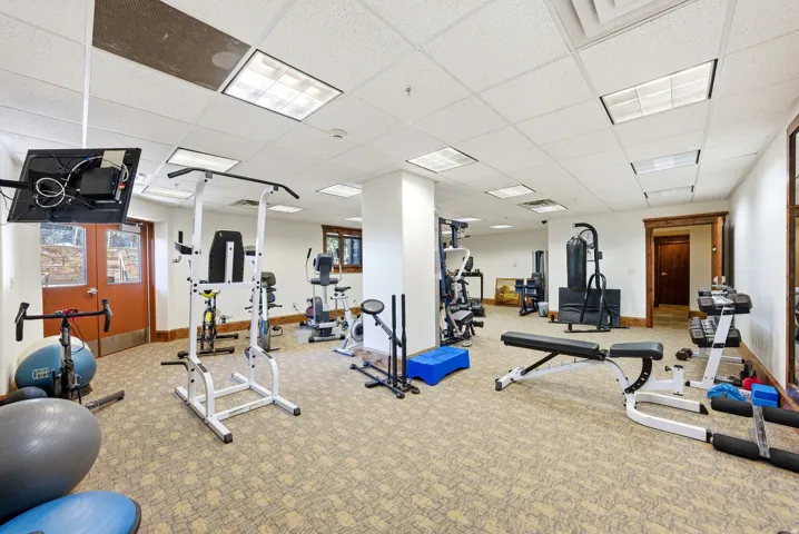 Spacious fitness room featuring patterned carpeting, recessed lighting, a drop-panel ceiling, and multiple workout equipment stations
