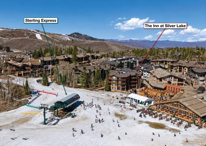 Aerial view of a ski resort community featuring multiple multi-story buildings with varied architectural styles, a ski lift, and mountain terrain in the background