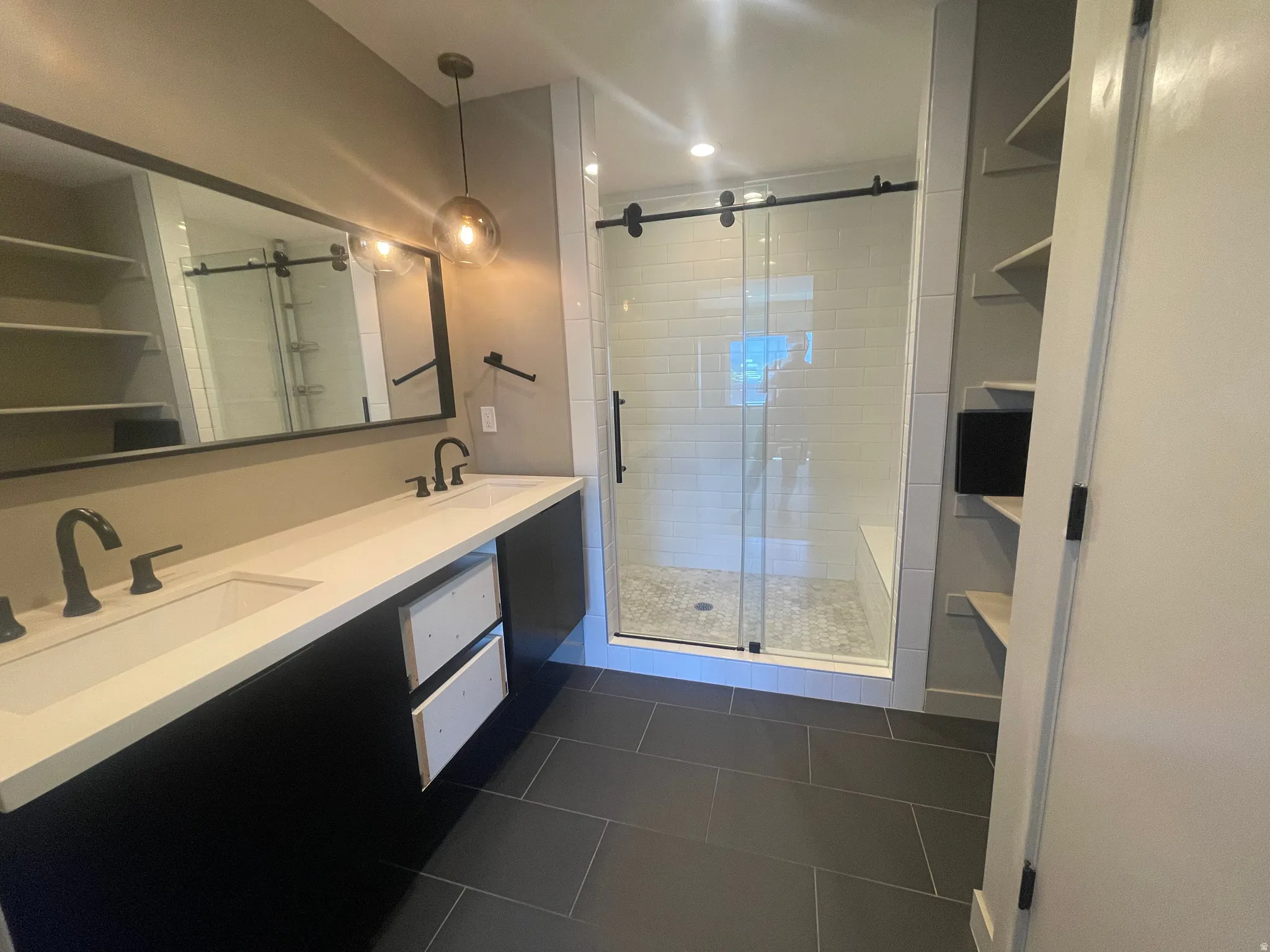 Primary bathroom Spacious bathroom featuring a dual vanity with a white countertop and matte black faucets, a large walk-in shower with subway tile and a bench, a rectangular mirror, and open shelving