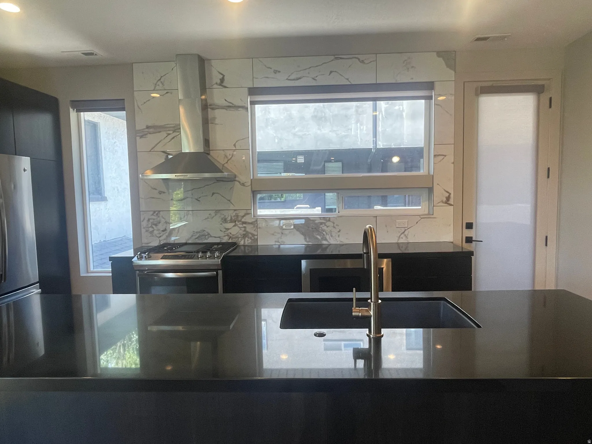 Contemporary kitchen featuring black countertops, a stainless steel range hood, a gas range, a built-in microwave, and a black undermount sink with a gold-tone faucet