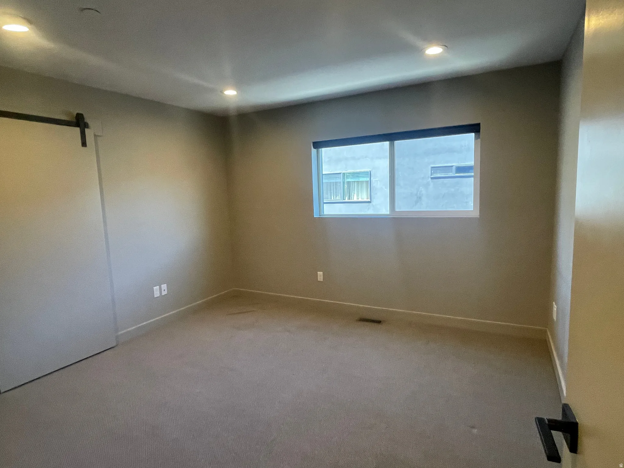 Carpeted room featuring a modern barn door, recessed lighting, and a single window with a roller shade