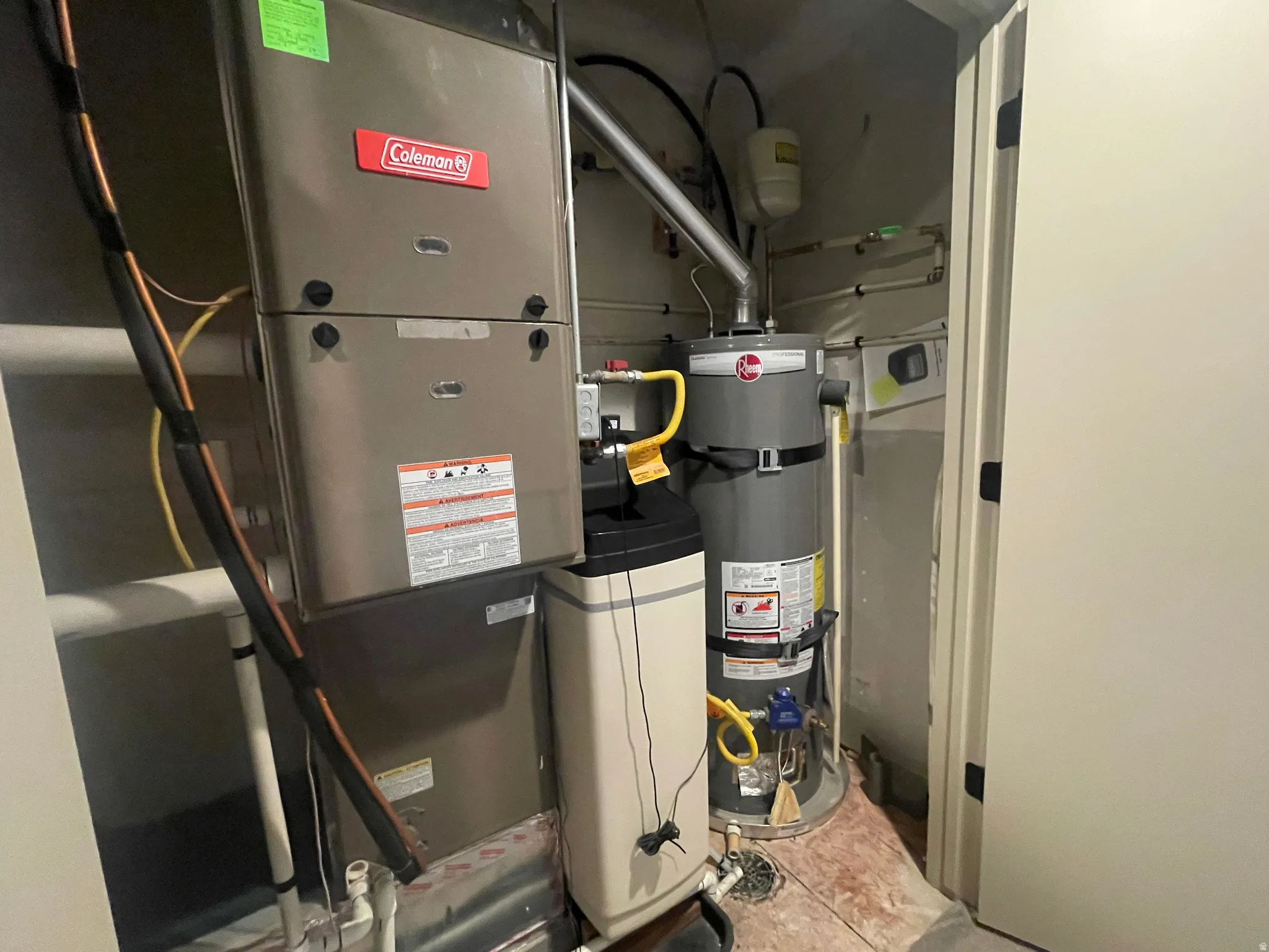 Dedicated utility closet featuring a Coleman furnace, Rheem water heater, water softener system, and integrated floor drain