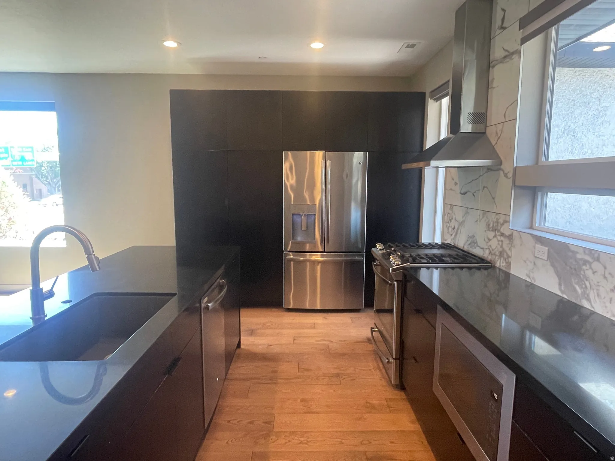 Contemporary kitchen featuring dark cabinetry, stainless steel appliances, and wood-finish flooring