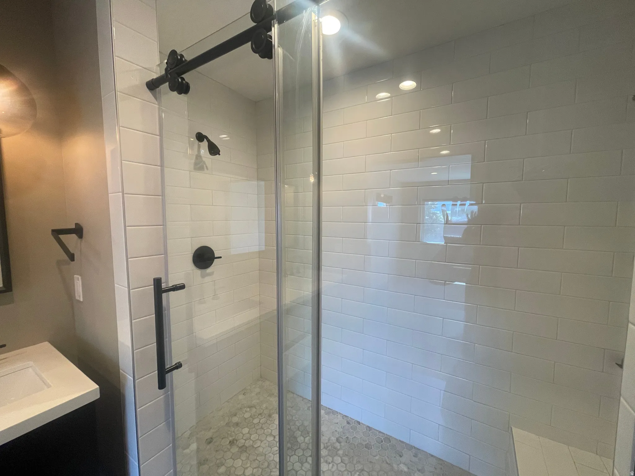 Primary bathroom Shower enclosure featuring a glass barn door, white subway tile walls, a built-in bench, and a pebble-finish floor