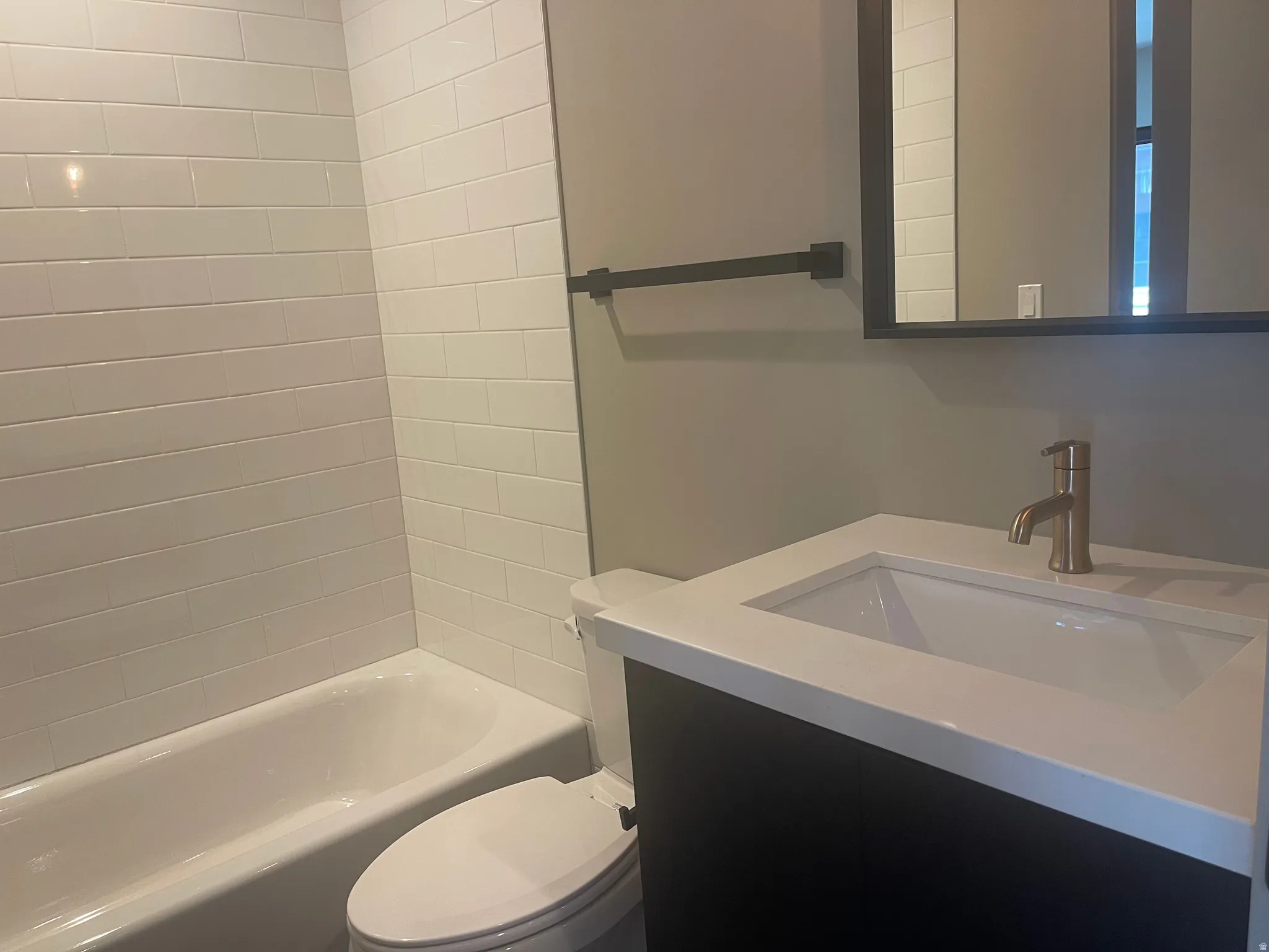 1st floor Bathroom featuring a white subway tile tub surround, dark wood-finish vanity with an integrated white sink, brushed bronze single-handle faucet, and a wall-mounted medicine cabinet with a black frame