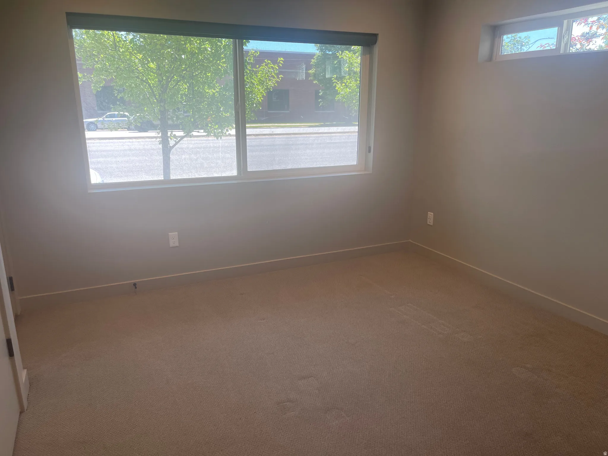 1st floor bedroom Neutral wall paint with carpet flooring, featuring a large window with roller shades and an upper transom window