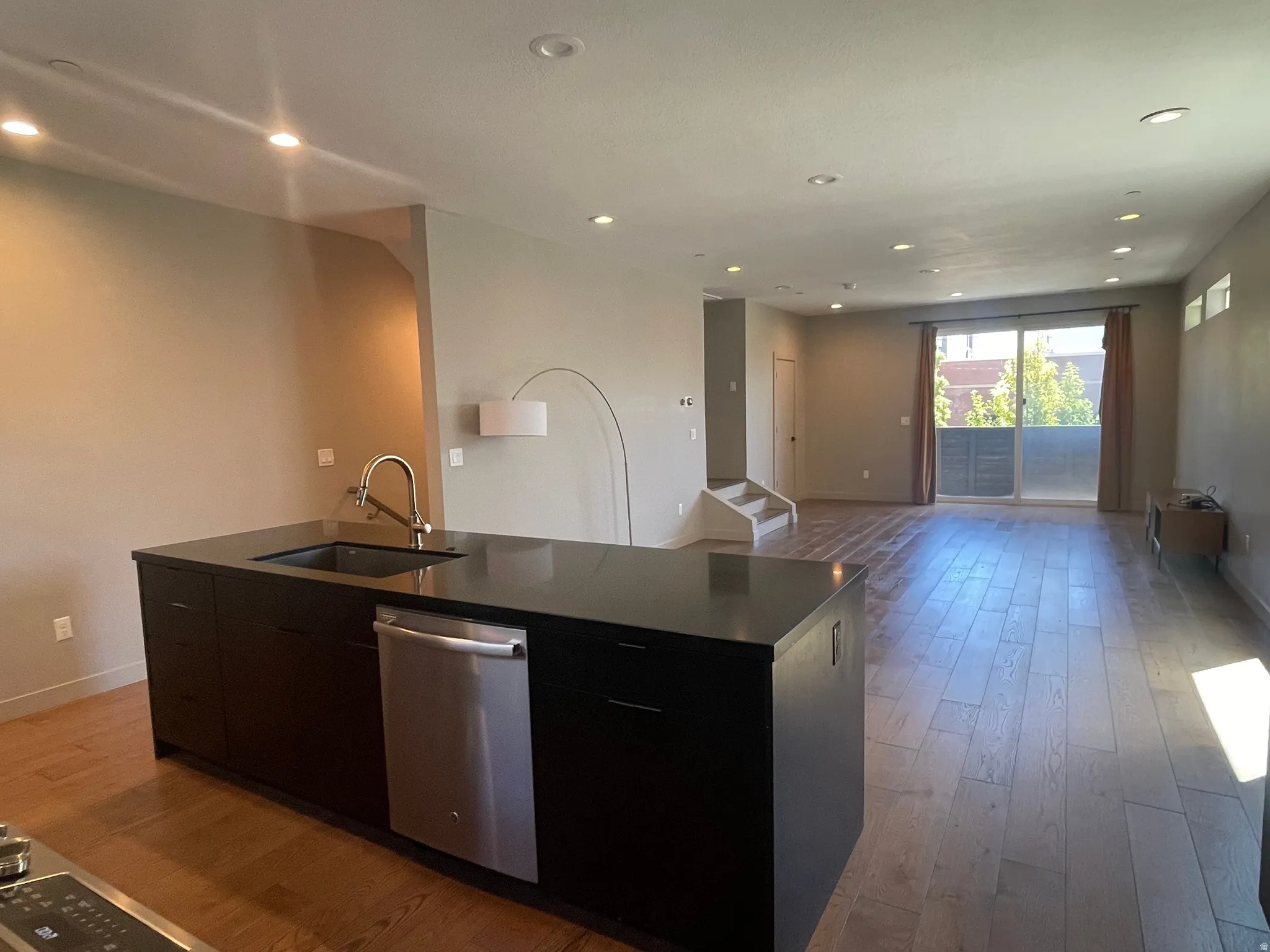 Open-concept living area featuring wood-finish flooring, recessed lighting, and a kitchen island with an integrated sink and stainless steel dishwasher