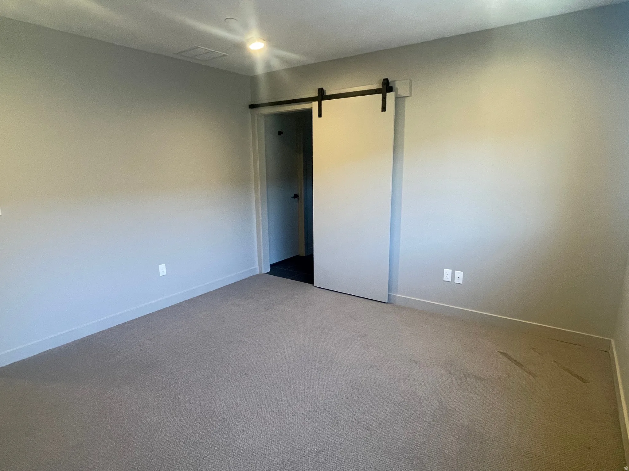 Spacious room featuring neutral carpeting, light gray wall finishes, recessed lighting, and a modern barn door entry