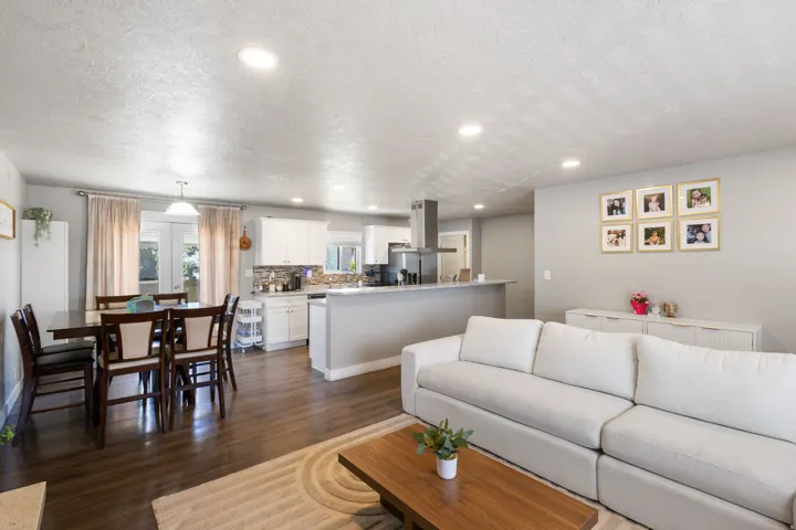 Open-concept living area featuring dark wood-finish flooring, recessed lighting, a kitchen with white cabinetry, a kitchen island with a breakfast bar, and a dining area with a pendant light fixture