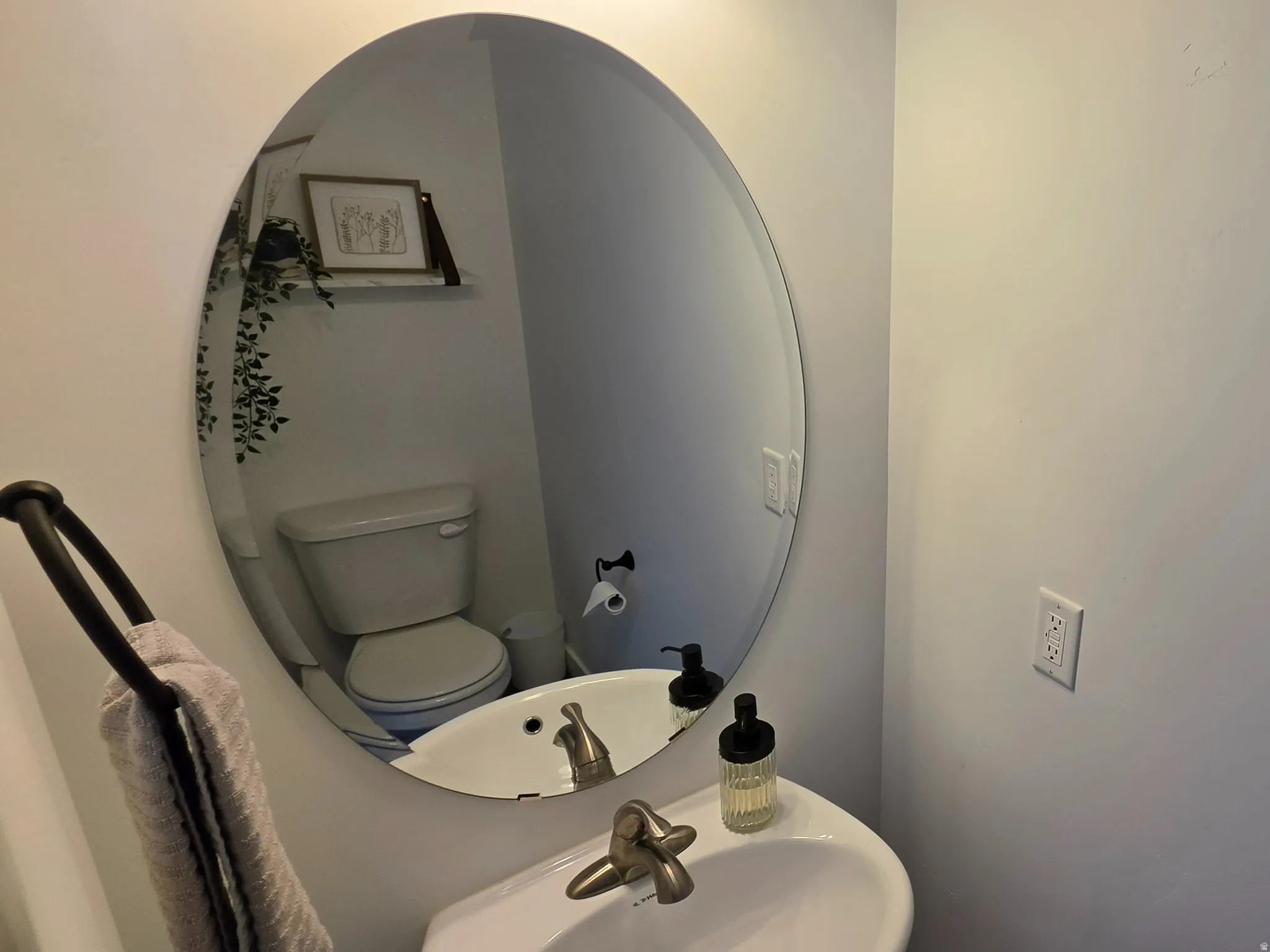Pedestal sink with a brushed nickel faucet, large oval mirror, and a wall-mounted toilet