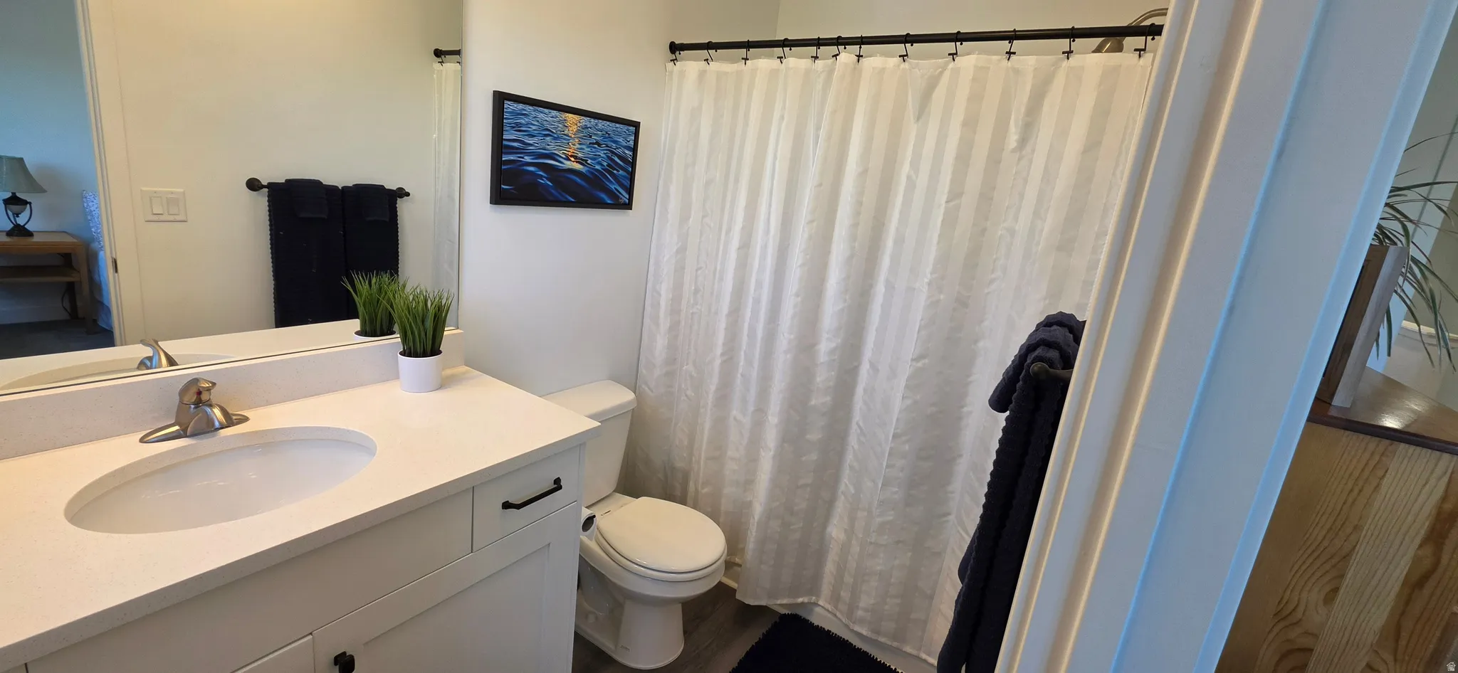 Modern bathroom featuring a single vanity with an integrated sink, a large mirror, and a white shower curtain with a black rod