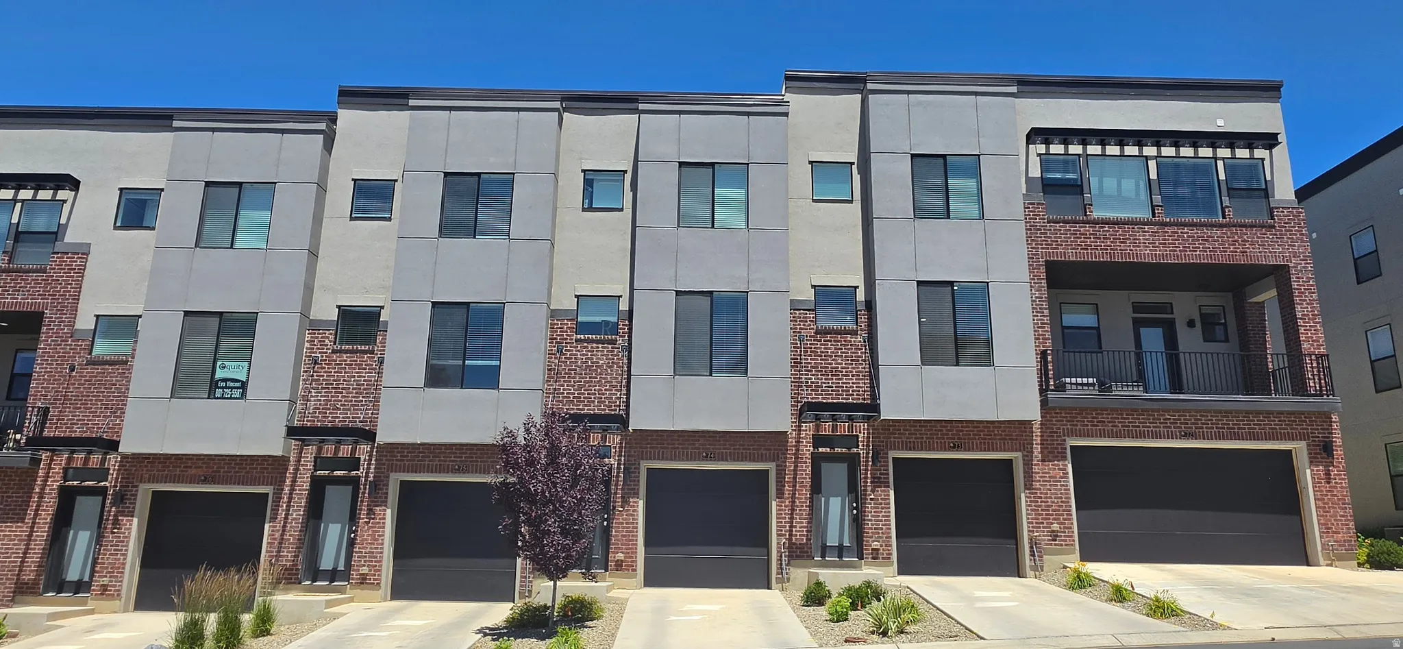 Modern townhome exteriors featuring red brick accents, light gray siding, black framed windows, and individual garage doors