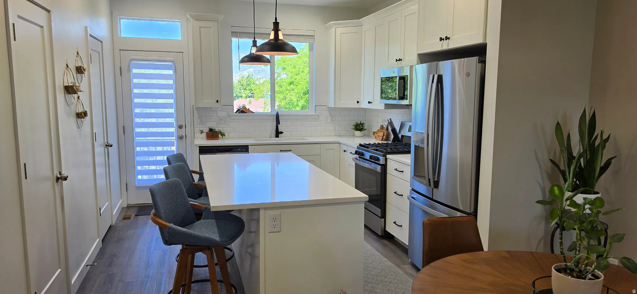 Modern kitchen featuring a central island with countertop seating, white shaker cabinetry, stainless steel appliances, and wood-finish flooring