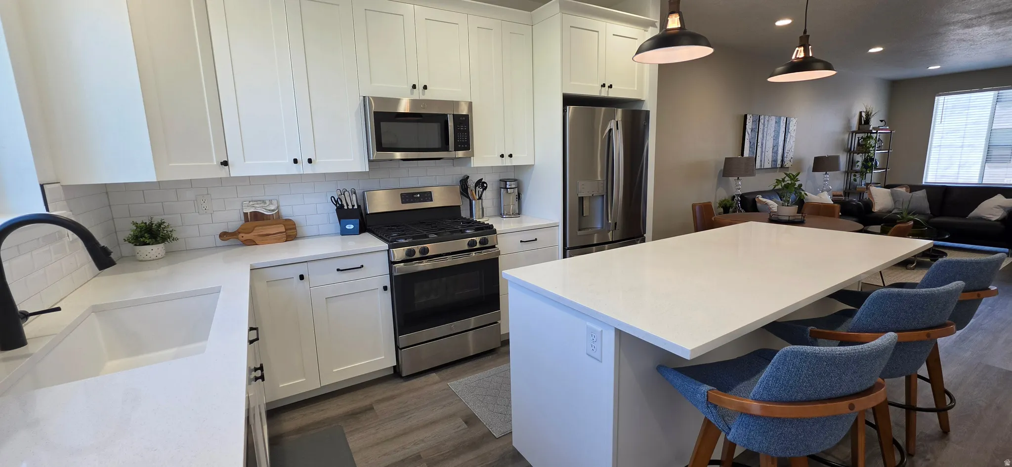 White shaker cabinetry with dark hardware, stainless steel appliances, light-toned countertops, subway tile backsplash, and wood-finish flooring