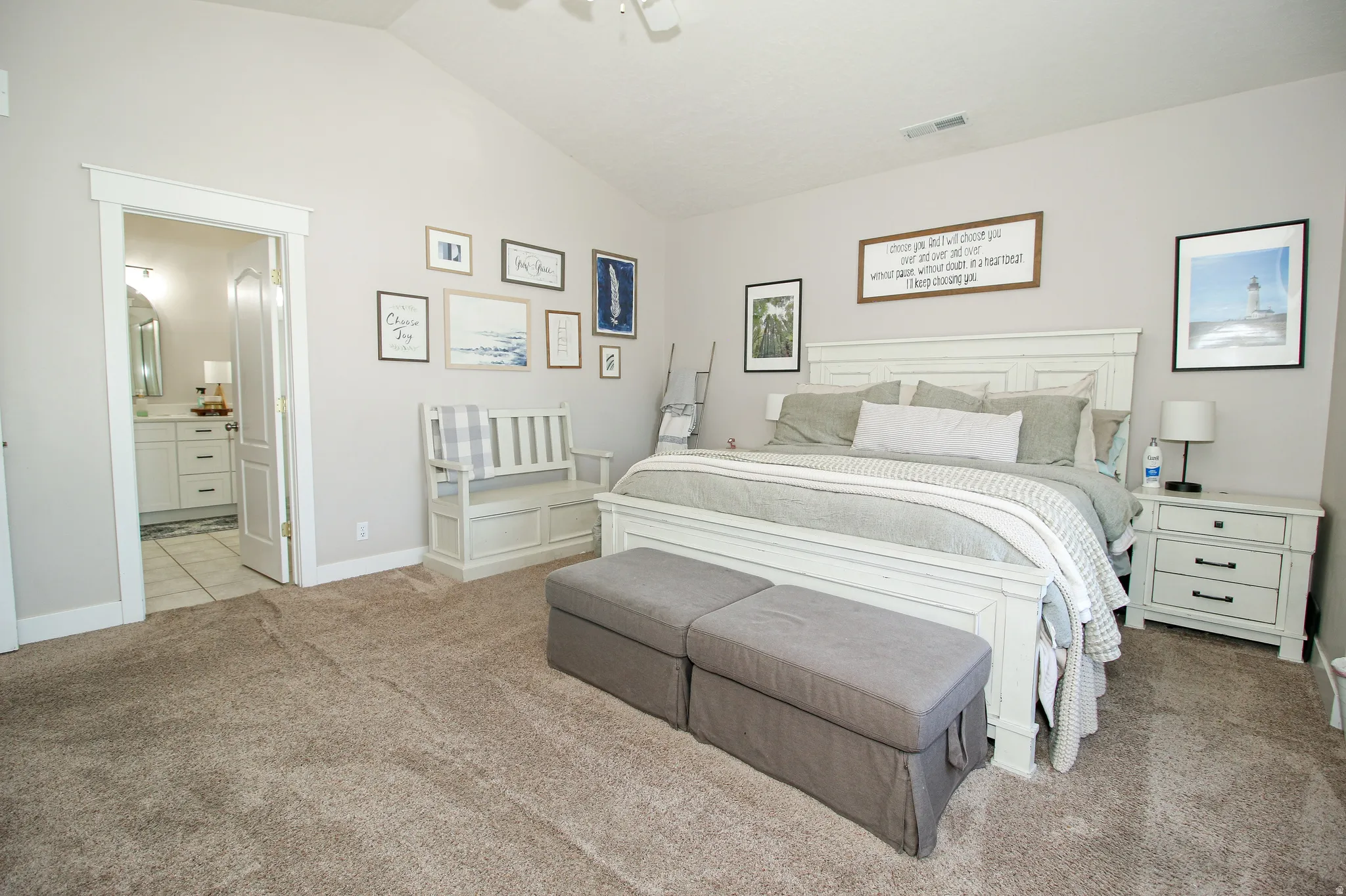 Carpeted bedroom featuring vaulted ceilings, a white paneled headboard, and an en-suite bathroom entry