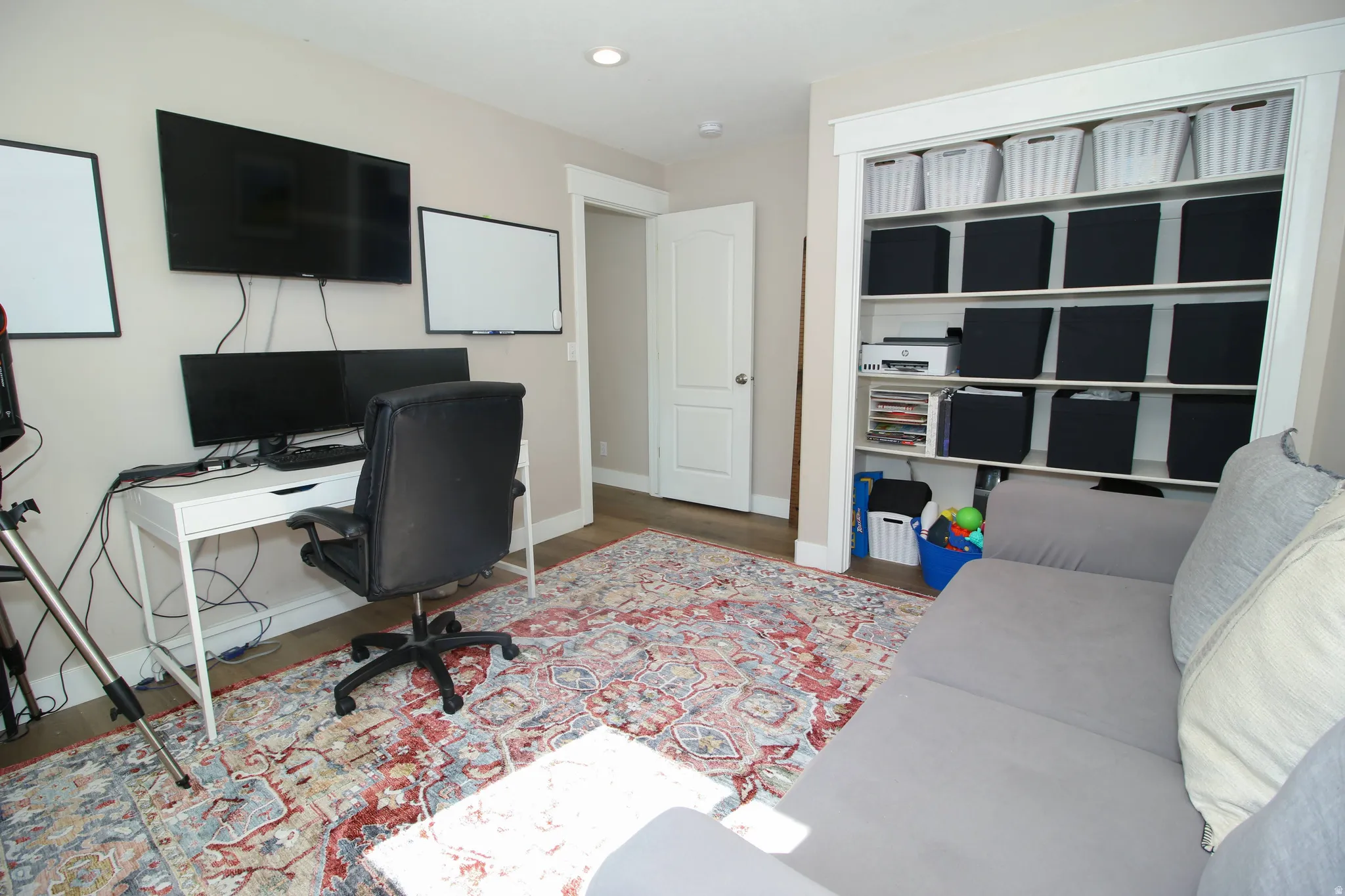 Versatile room featuring an integrated built-in shelving unit, neutral wall color, and wood-finish flooring