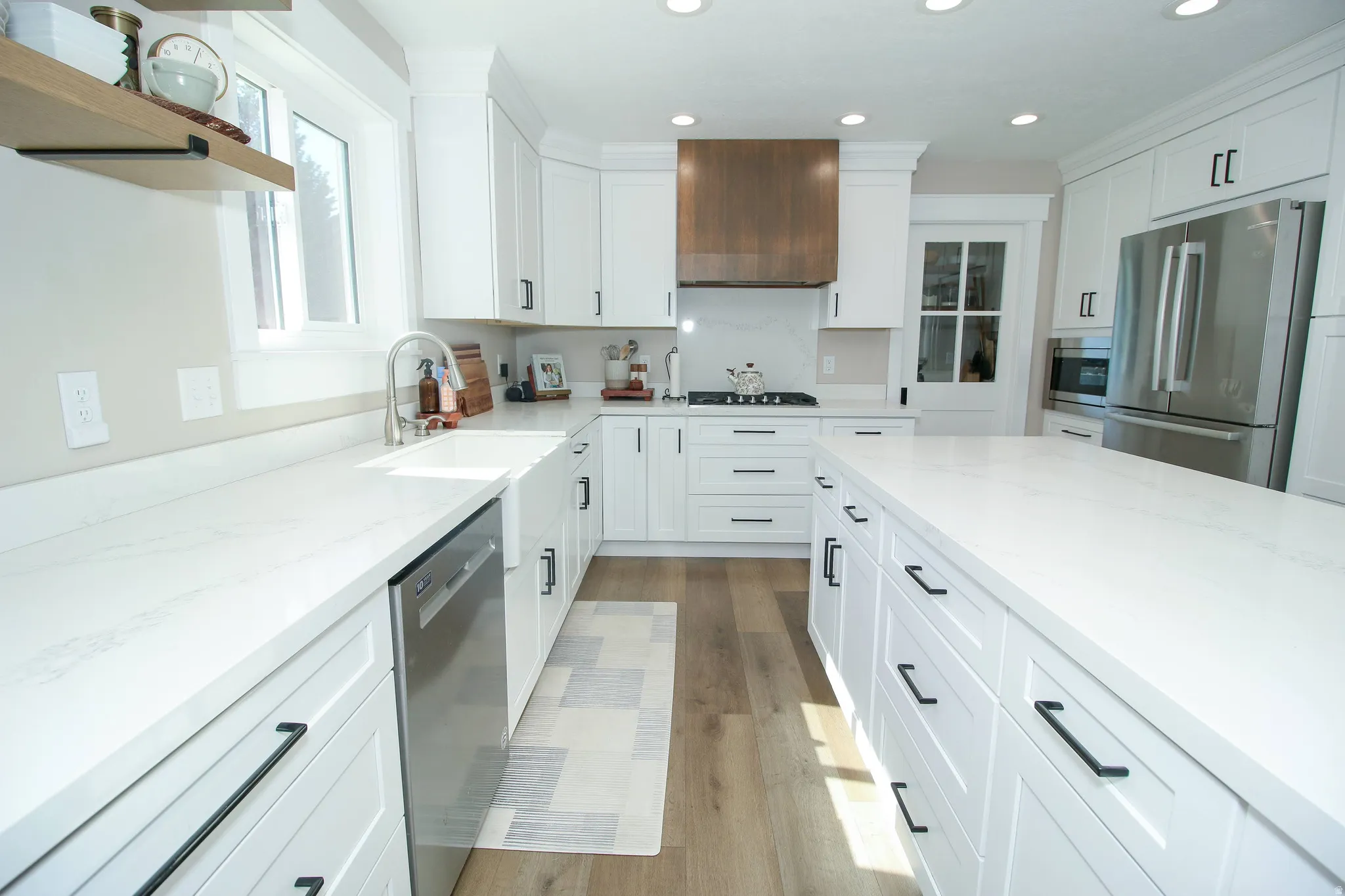 Spacious kitchen featuring white cabinetry, light countertops, wood-finish flooring, stainless steel appliances, and a central island