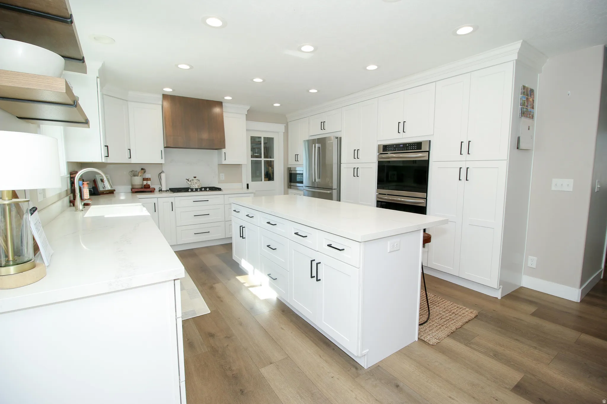 Spacious kitchen featuring white shaker cabinetry, an expansive center island, integrated stainless steel appliances, wood-finish flooring, and recessed lighting