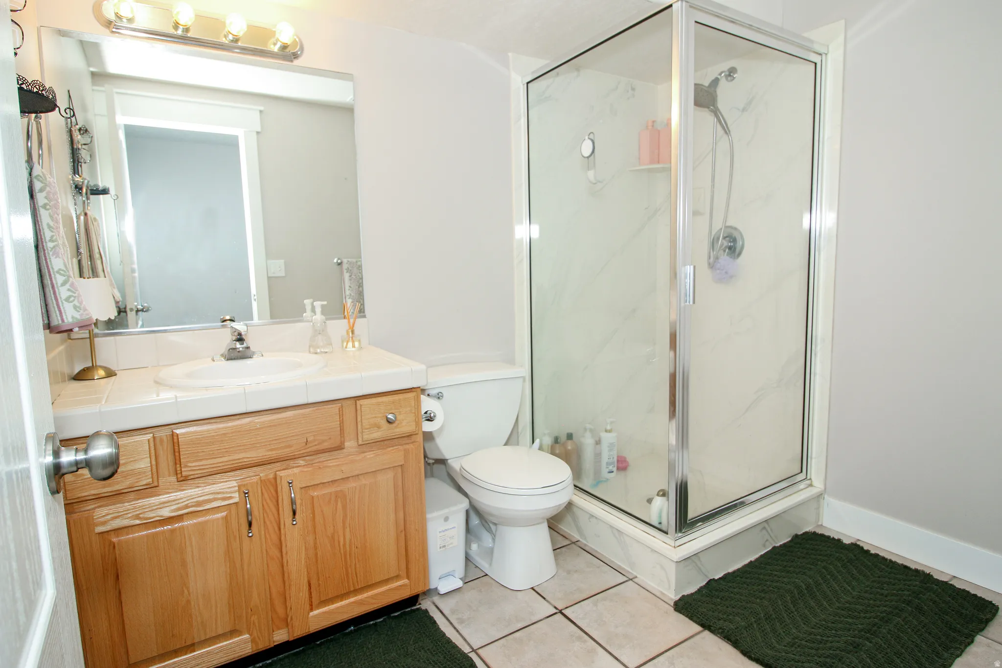Bathroom featuring a wood-finish vanity with a tile countertop, a framed mirror, and a four-light vanity fixture