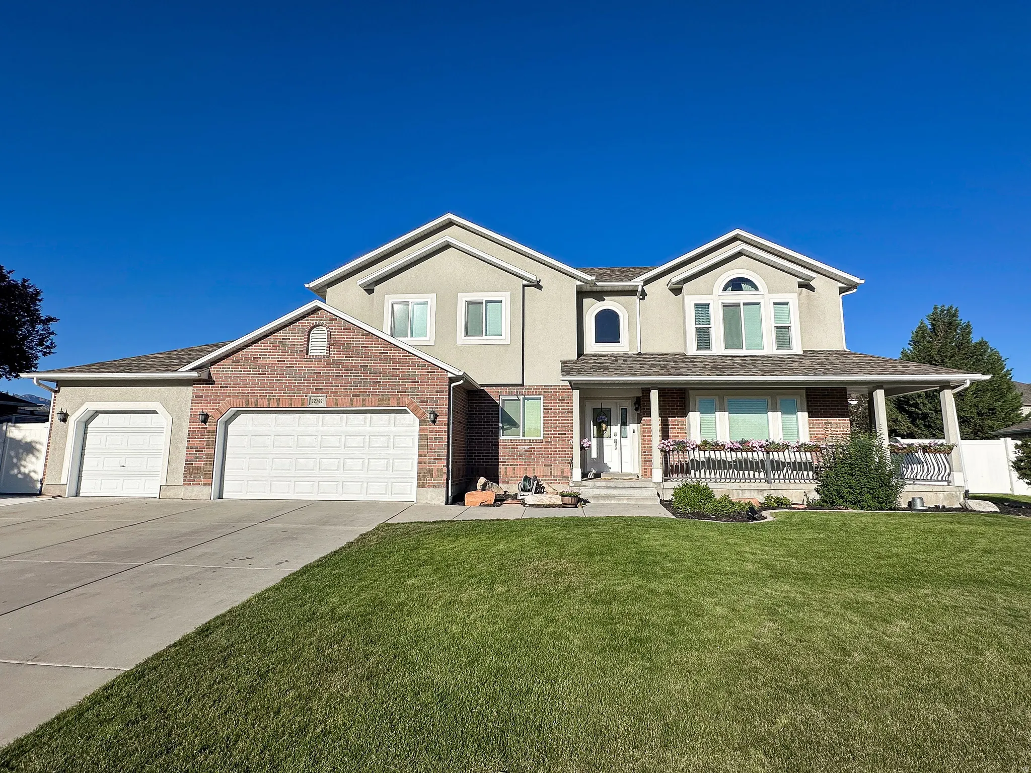 Two-story stucco and brick exterior featuring a covered front porch with decorative railing, dual garage doors, and arched windows