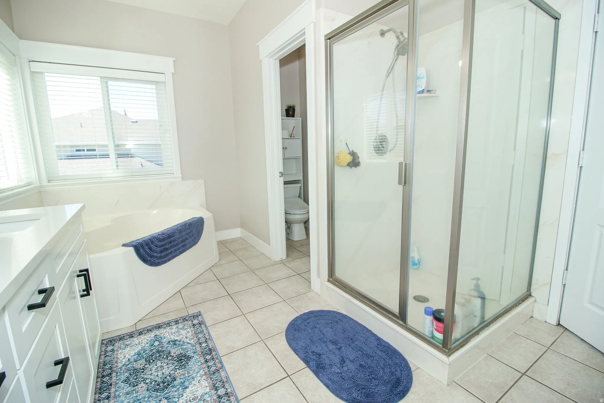 Bathroom featuring a glass-enclosed shower, corner soaking tub, and dual-sink vanity with white cabinetry and dark hardware