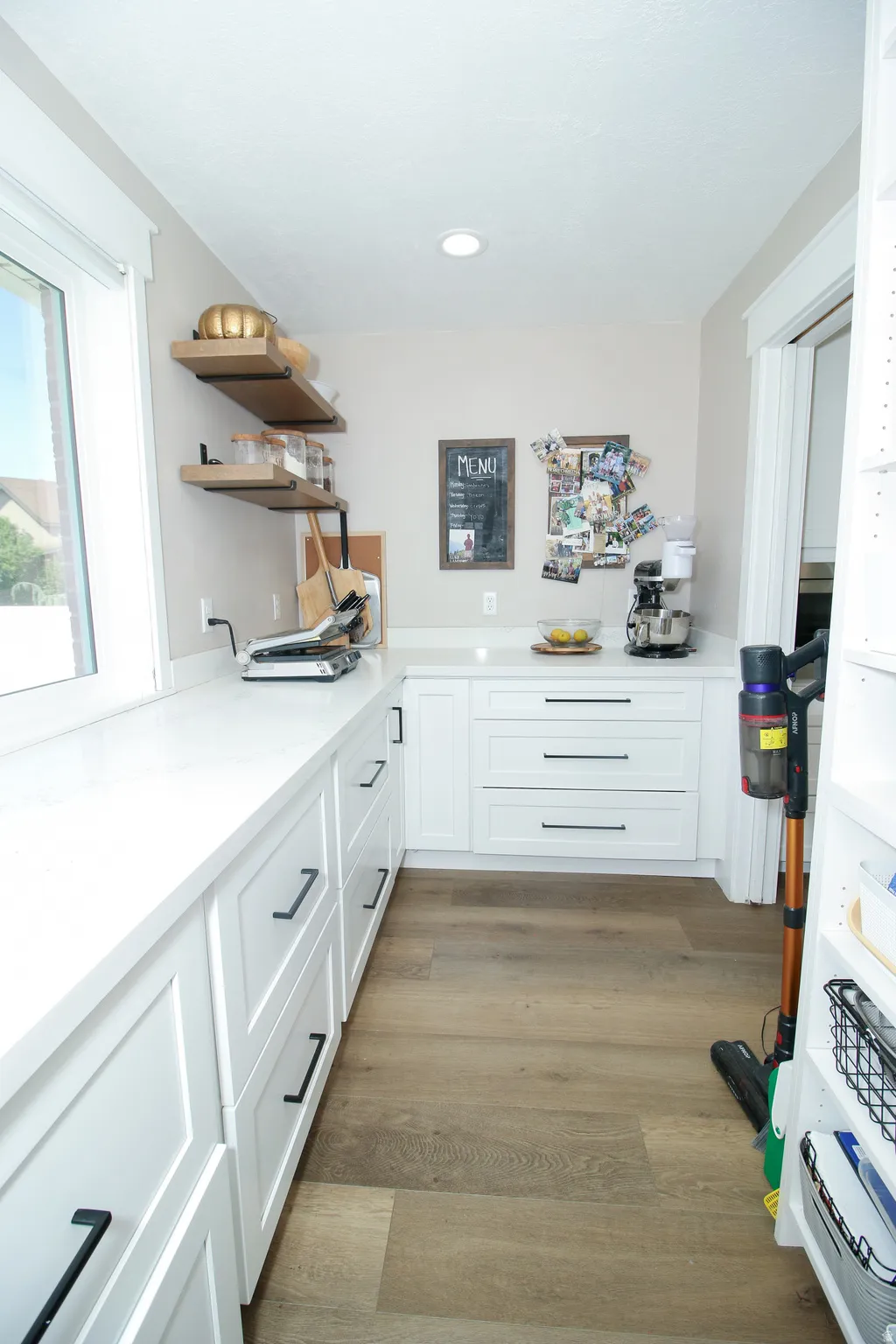 Spacious kitchen prep area featuring extensive white cabinetry, quartz countertops, wood-finish flooring, a large window, and open shelving