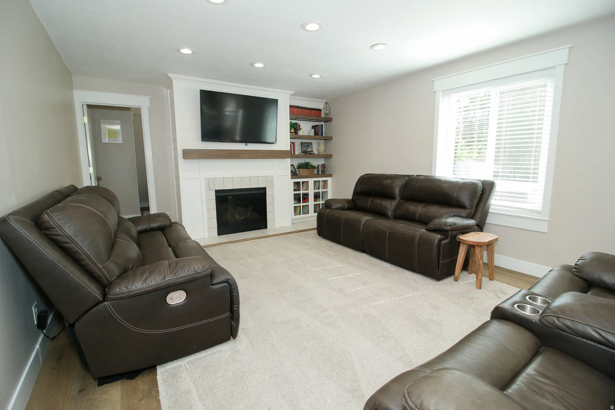 Living area featuring a fireplace with a white tile surround and wood mantel, built-in shelving, recessed lighting, and wood-finish flooring