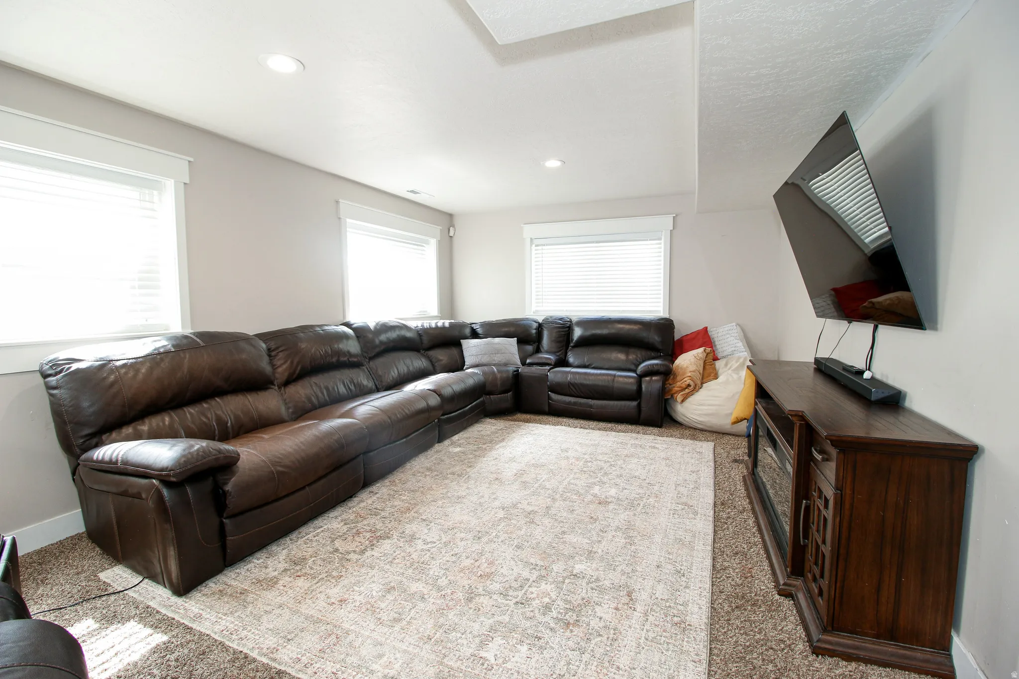 Recessed ceiling lighting illuminates this versatile space featuring light-toned walls and two windows with white blinds