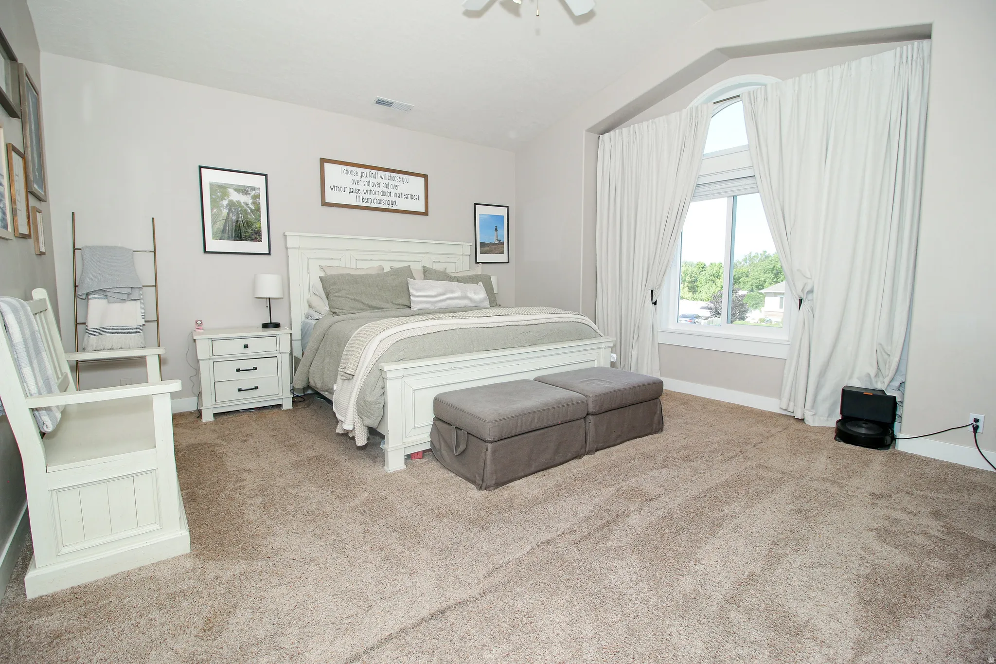 Carpeted room featuring a large arched window with white trim, a ceiling fan, and painted walls