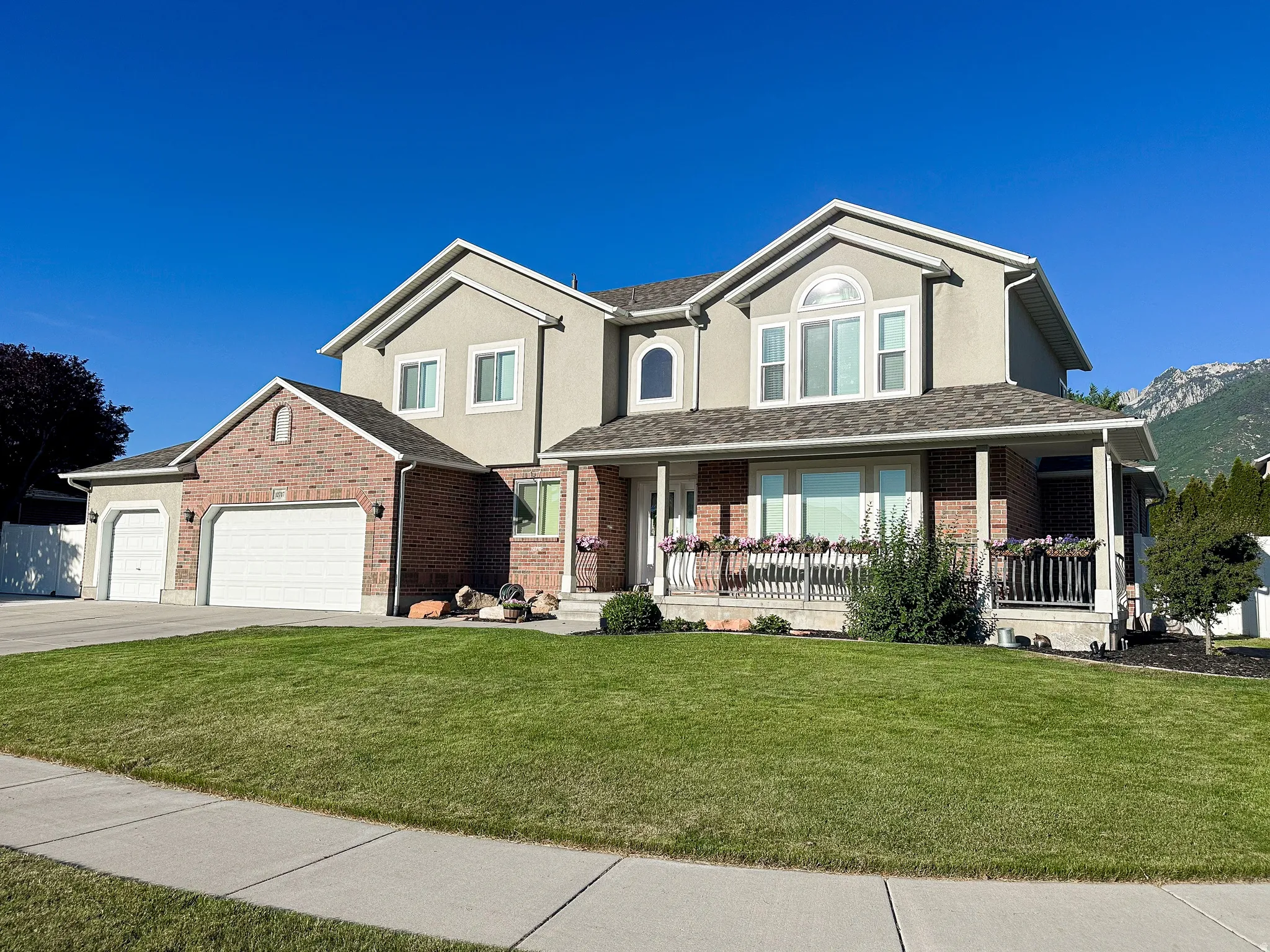 Traditional-style residence featuring a combination brick and stucco exterior, an attached multi-car garage, and a covered front porch with a white railing