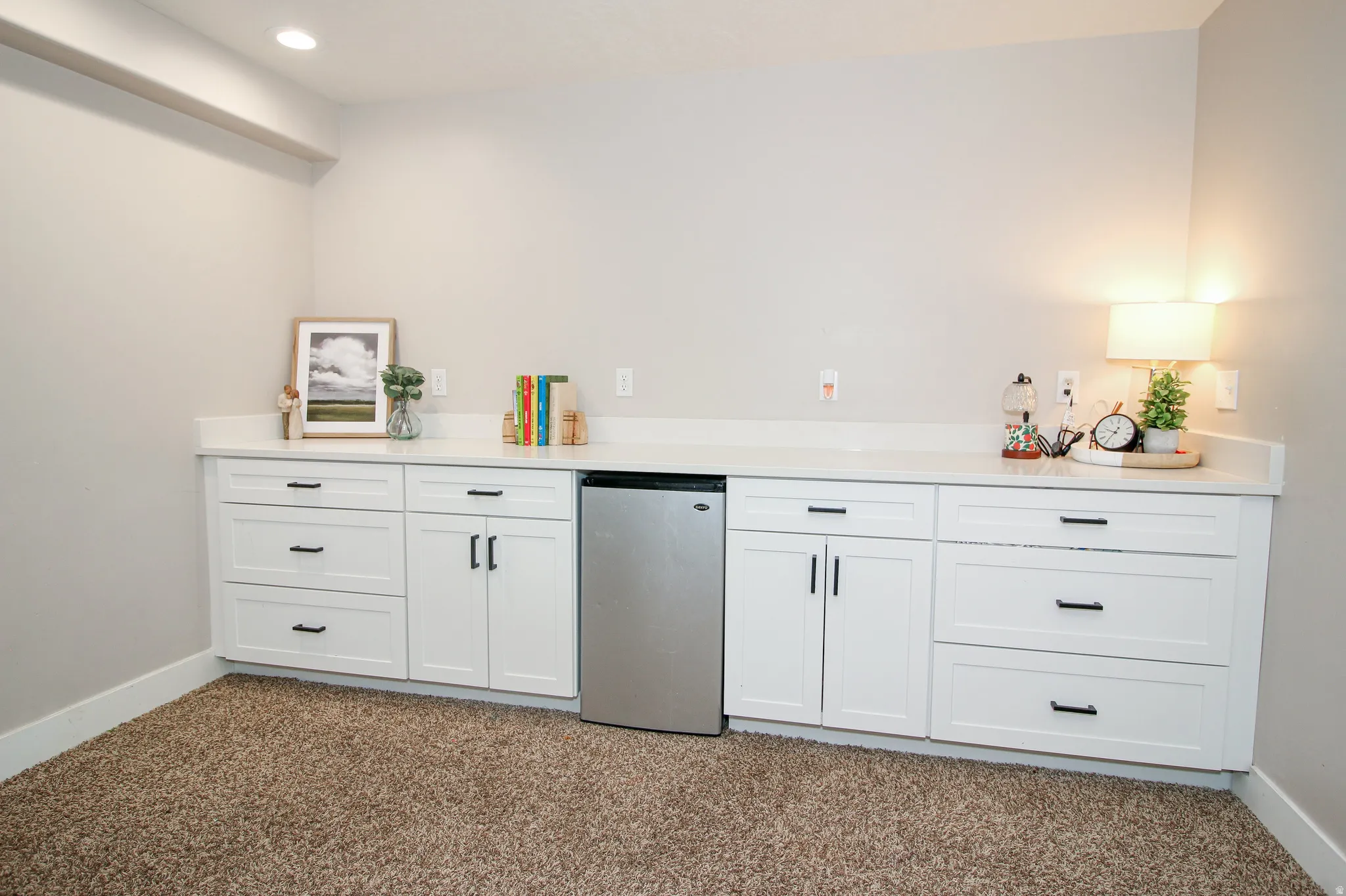 Built-in cabinetry featuring a stainless steel beverage refrigerator, white Shaker-style doors, black hardware, and a light-toned countertop