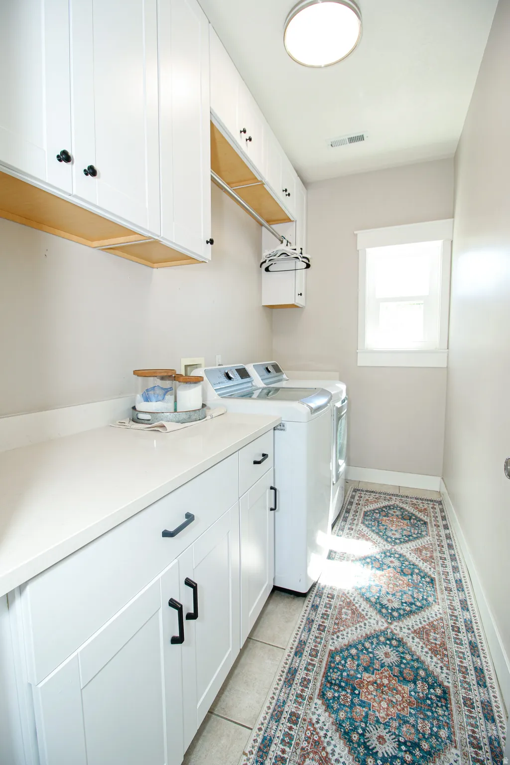 Laundry room featuring extensive white cabinetry, light-toned countertops, and tile flooring