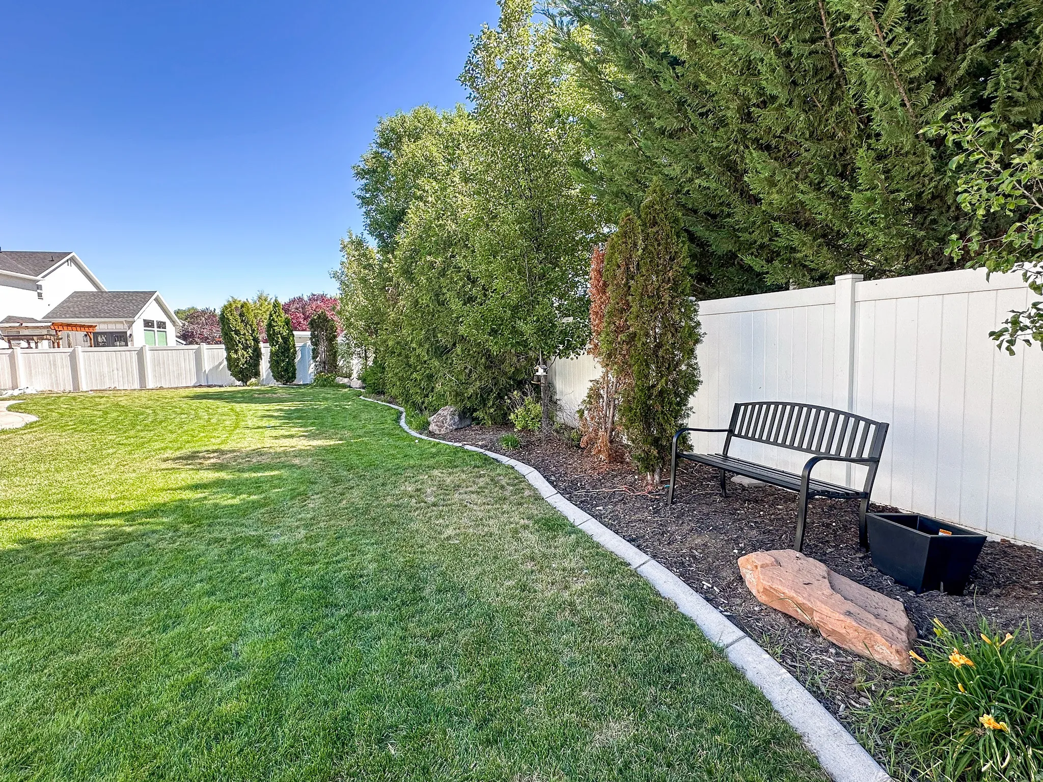 Expansive lawn bordered by a white vinyl fence and mature perimeter trees