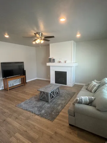 Living area featuring wood-finish flooring, a contemporary fireplace with a white mantel, and recessed ceiling lighting