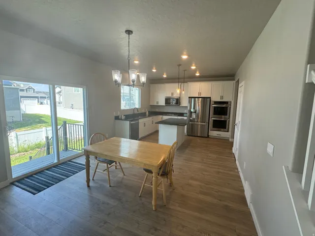 Open-concept kitchen and dining area featuring wood-finish flooring, white cabinetry, dark countertops, and stainless steel appliances