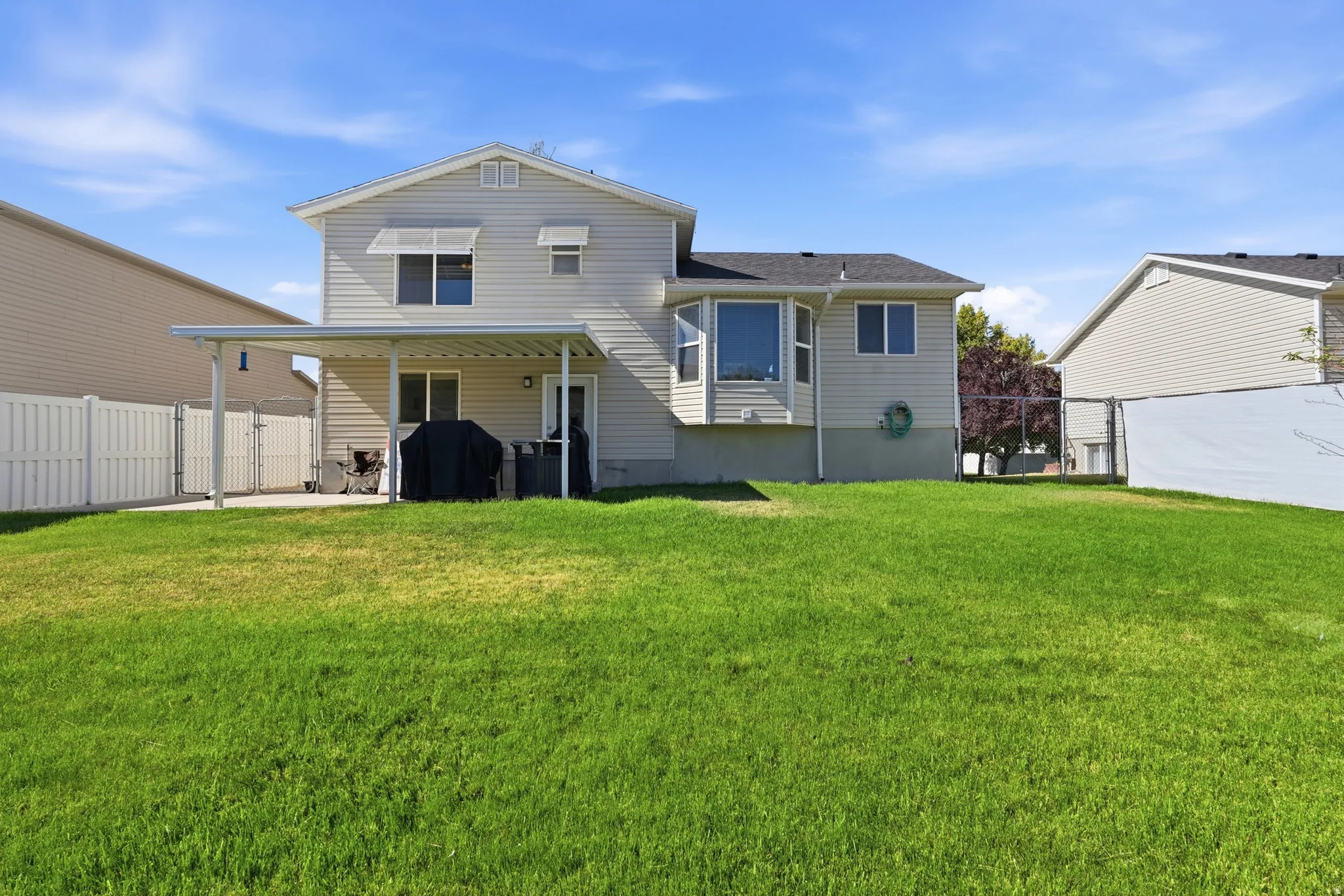 Expansive green lawn extending from a covered patio structure, featuring a bay window on the rear elevation, horizontal siding, and a privacy fence